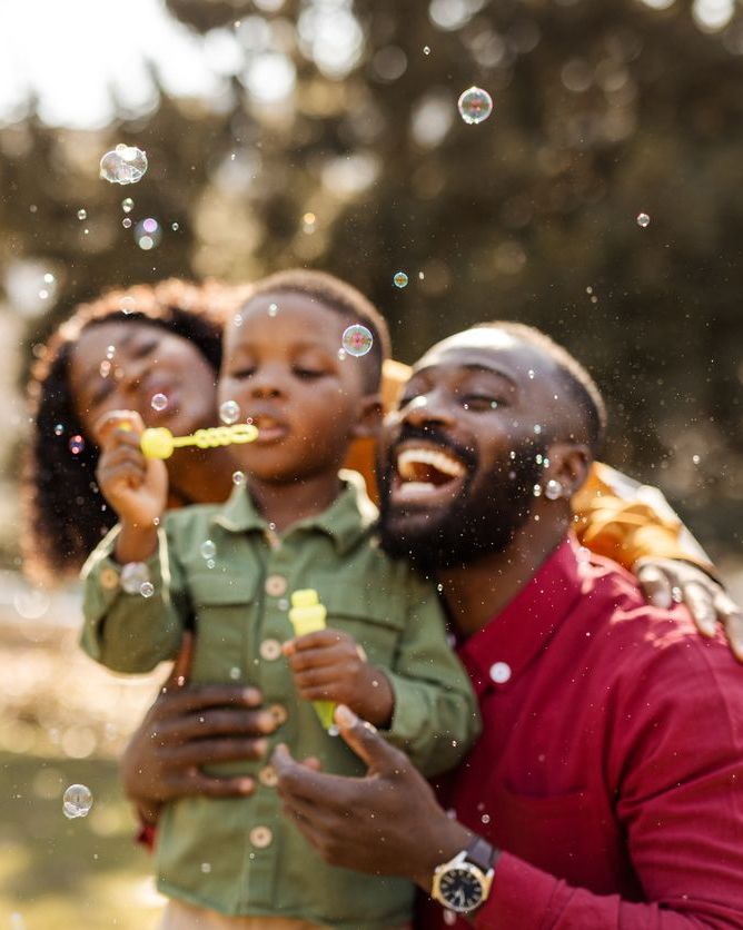 Happy African American Family Blowing Bubbles Outdoors Achieve your best smile at Gunnerson Dental